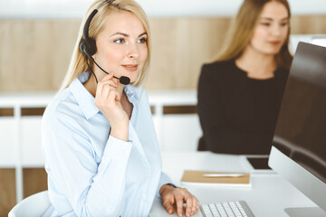 Blonde business woman sitting and communicated by headset in call center office. Concept of telesales business