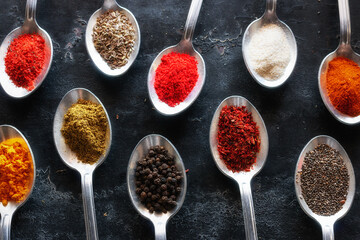 spices and herbs in tablespoons on a black kitchen table close-up