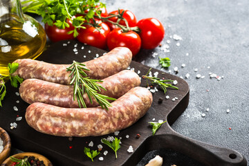 Bratwurst or sausages on cutting board with spices at black table.
