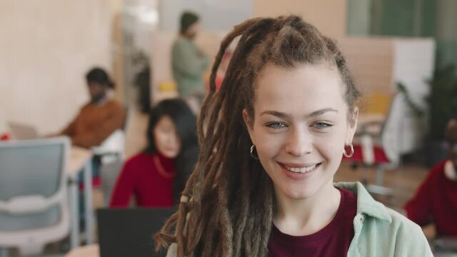 Portrait of happy young businesswoman with dreadlocks smiling for camera in open-plan office or coworking space