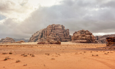 Rocky massifs on red orange sand desert, overcast sky in background - typical scenery in Wadi Rum, Jordan