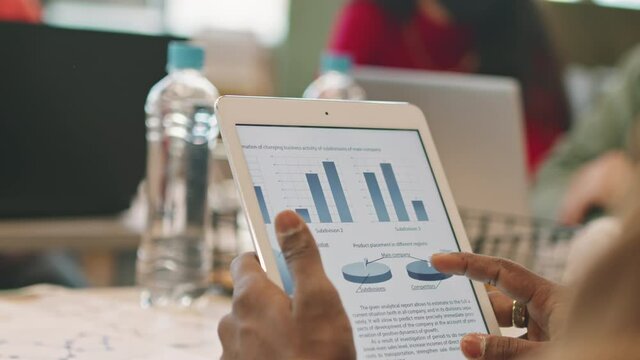 Close up shot of unrecognizable businessman holding tablet and studying financial document during meeting