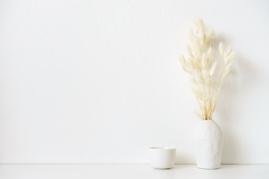 Eine Tasse und eine Vase mit Trockenblumen auf einem weißen Tisch. Wand, Inneneinrichtung, modern.