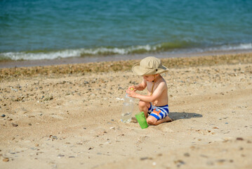 A small boy alone plays on the seashore, wearing a hat and striped shorts. Heat