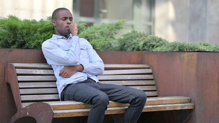 Sick Young African Man Coughing on Bench Outdoor