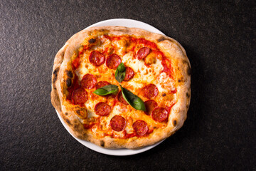 pizza alla diavola with spicy salami, mozzarella, tomato and basil. view from top. black stone...