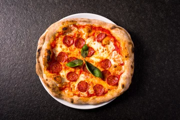 Fototapeten pizza alla diavola with spicy salami, mozzarella, tomato and basil. view from top. black stone background © Luca