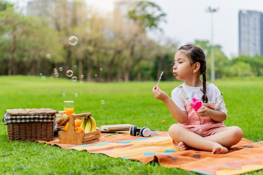 Happy little girl kid blowing soap bubbles playing alone in the park, Black hair style