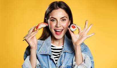 Happy woman shows sashimi and makizushi. Girl eating sushi rolls with chopsticks and smiling from amazing discounts for takeaway in japenese restaurant. Female student order lunch in delivery app