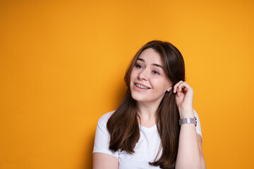 Smiling young girl in a white T-shirt with braces tucking her hair behind her ear and looking away