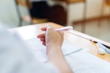 Hand female asian student reading document exercise and taking exam test at classroom in high school. Concentration of teenager notes for SAT PISA evaluation measurement educational admission concept