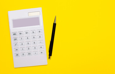 A white calculator and a black pen lie on a yellow background. Copy space