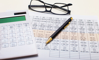 Against the background of the reports, a pen, a white calculator, and black-framed glasses. Business concept. Workplace close up