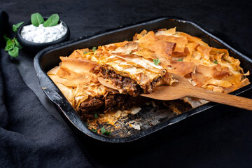 Traditional spiced Moroccan lamb ragout with filo pie served as close-up in a rustic black backing dish on a board © HLPhoto