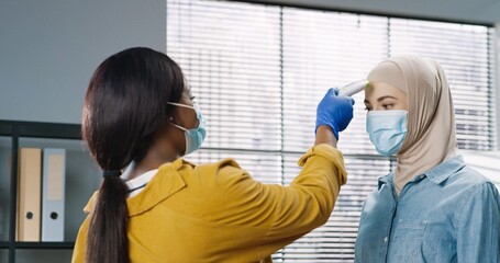 Rear of African American female in medical mask standing at office checking workers health...