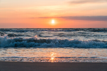 Orange sunset at the beach with sand and waves in the forground and reflection in the shallow water