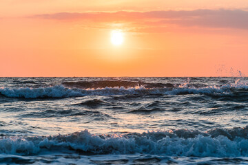 Obraz premium Close up of orange sunrise over the ocean with waves in the forground