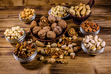 Various nuts (almond, cashew, hazelnut, pistachio, walnut) in bowls on a wooden table. Vegetarian meal. Healthy eating concept