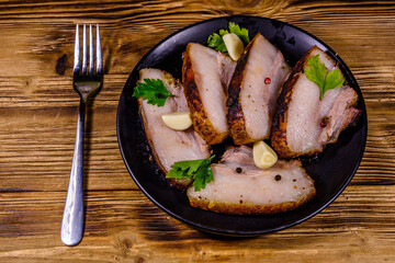 Slices of baked pork belly, garlic and parsley on a black plate