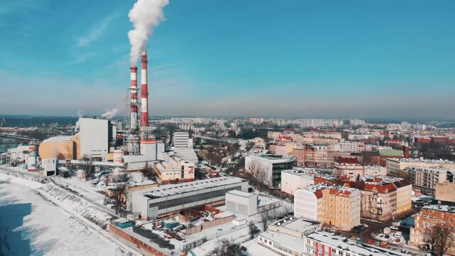 Industrial area of Wroclaw, Poland. Smoke coming out from the chimneys of the thermal power plant. Aerial view of the buildings in the city. Streets are covered with snow. Clear blue sky in the