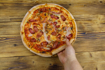 Hand taking a slice of tasty pizza. Hot italian pizza on wooden table. Top view