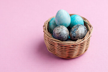 Easter. Painted quail eggs in a wicker basket on a pink background. banner with place for text, side view.