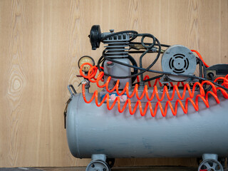 The small, gray air compressor has an orange hose stored on top of it. Was placed next to a wall...