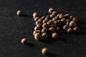 allspice black peppercorns, seasoning for food, sprinkled on gray background