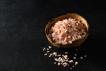 Fototapeta na wymiar pink himalayan coarse salt in a coconut bowl on dark gray background, empty space for text