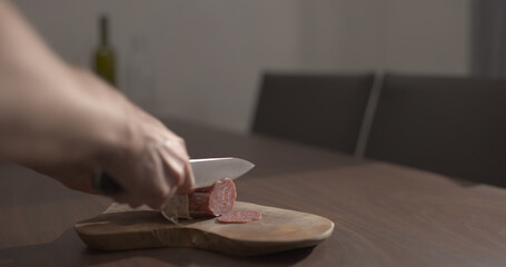 man slicing salame on olive wood board on walnut table