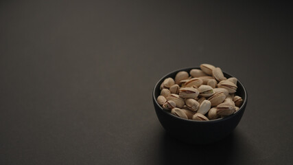 salted large pistachios in black bowl on black paper background