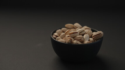 salted large pistachios in black bowl on black paper background