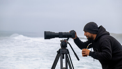 Surf photographer taking photos of the sea and surfers on a cloudy day with his camera and...