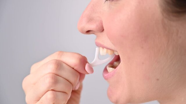 Caucasian woman brushing teeth with toothpick with dental floss on white background.