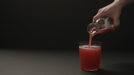 man hand pour berry drink into tumbler glass on black paper background with copy space