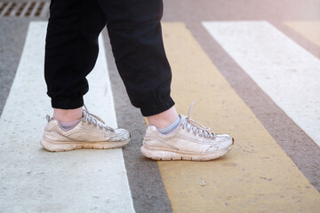 Feet of a girl in sneakers cross the road on a pedestrian crossing