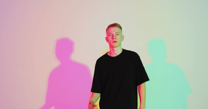 Stylish young guy cool moving in colorful neon studio light. Contemporary rap and hip hop youth culture