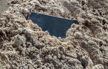 The remains of mobile phones with a broken screen that are garbage containing toxic substances that are harmful to the environment are left on the beach sand. Waste from Electrical and Electronic Equi