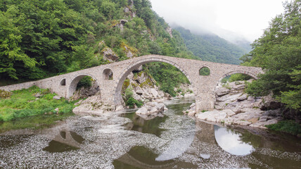 Fototapeta na wymiar Roman Old stronework,devil bridge, from the ottoman on eastern europe, at Bulgaria. Medieval structure over the river in rhodope. Aerial view with drone of Mystic bulgarian location. Balkans valley