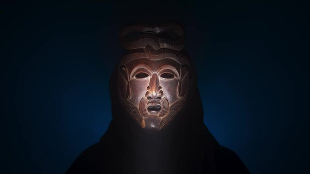 Creepy, masked cultist standing in a dark room. Scary horror scene, mysterious man in a tribal mask isolated on a black background. Eerie mask, devil concept.