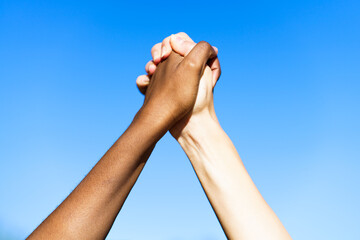 Multiethnic women's hands together against blue sky.