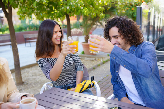 Couple of friends toasting while having a drink with their multi-ethnic group of friends