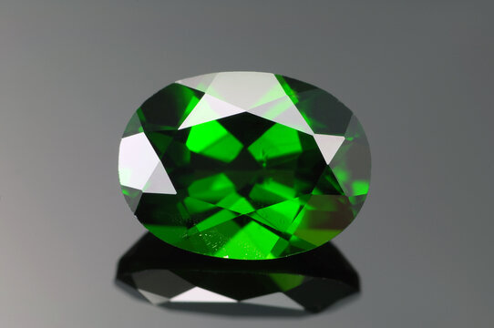 Natural bright bottle green color oval faceted chrome diopside loose gemstone. Transparent semiprecious stone setting for making jewelry. Gray gradient background. Close-up, macro.