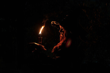 Silhouette of a witch woman with a torch and skull