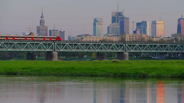 Panorama Warszawy w słoneczny dzień znad Wisły z okolic Żerania. Pociąg osobowy na moście kolejowym nad Wisłą przy stacji Warszawa ZOO