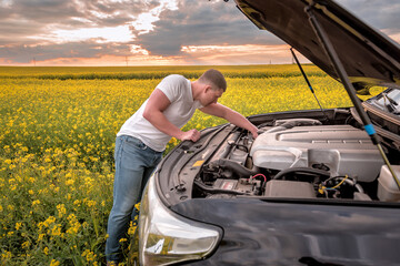man looks at the car engine in the field