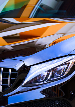 Samutsakhon,Thailand-January08,2021: Close up headlight with colorful reflection of building and blue sky on bonnet surface of black Mercedes-Benz C43 AMG car in vertical frame, illustrative editorial
