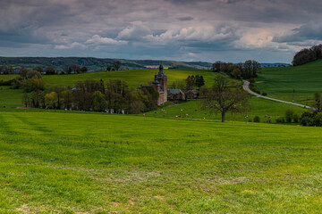 Fototapeta na wymiar 13th century castle in the rolling hill landscape and green meadows in Belgium with winding roads and a dramatic sky.