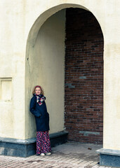 Fototapeta na wymiar A blonde woman in a black coat stands under an arch