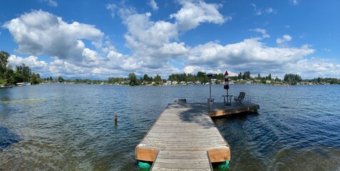 Panorama of Lake Stevens, Washington with a dock in the middle foreground, lots of clouds in a blue...